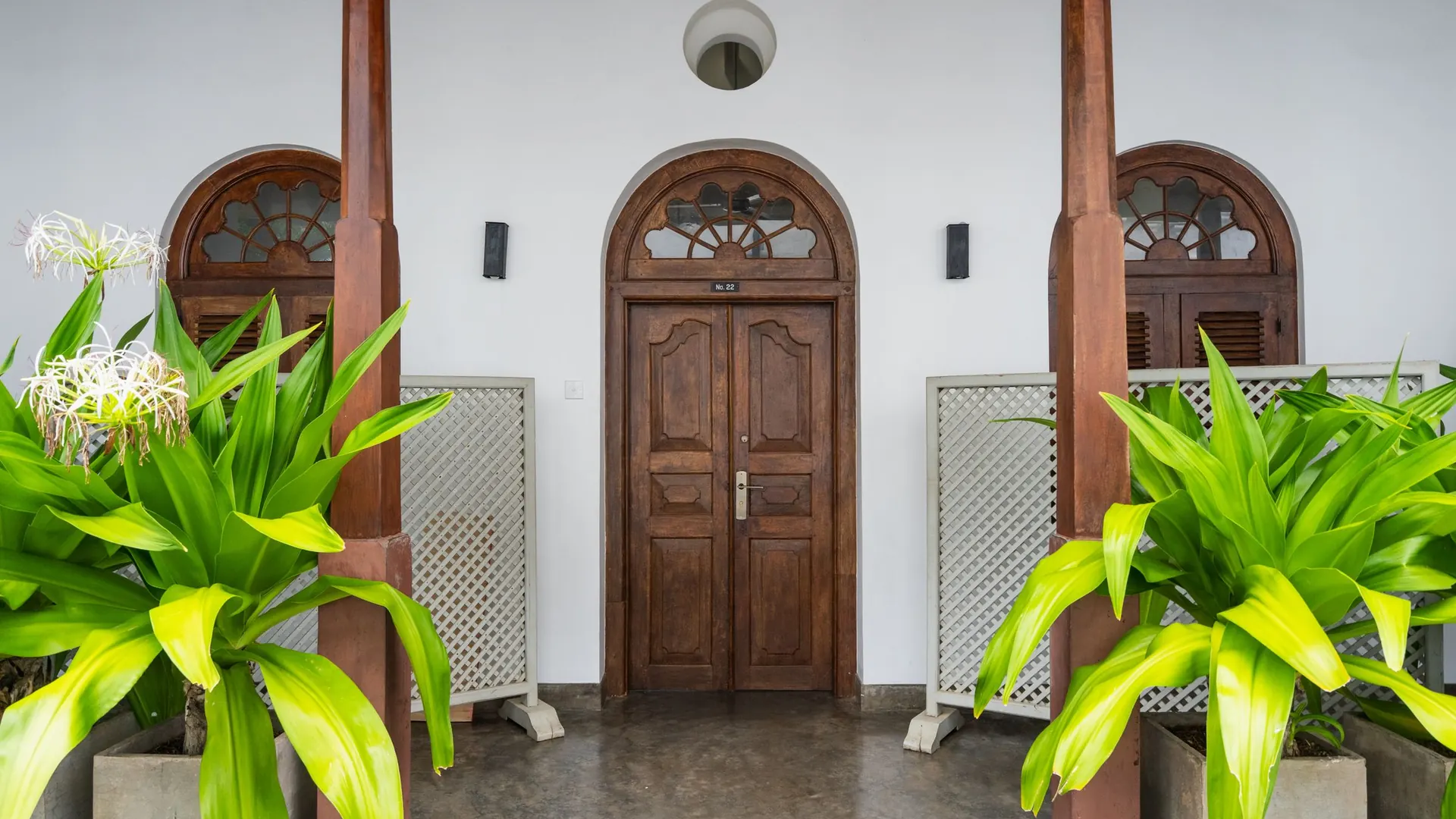 Pintu kayu di teras depan diapit tanaman hijau